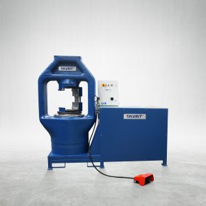Talurit® A blue industrial machine named "1000T - Swager," designed for the mechanical splicing of wire rope, features a cylindrical upper section and a control panel on the side. Marked with "TAURT," it includes a foot pedal connected by a cable. The machine stands on a plain white floor against a neutral background. © Copyright Talurit AB. All rights reserved.