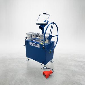 A blue and silver AV 30 - Annealing Machine from Talurit® is positioned on a concrete floor, designed for cutting wire rope. The machine features metal components and a circular handle on the side. A red foot pedal is connected to it with a black cable, lying on the floor in front of this wire rope equipment. © Copyright Talurit AB. All rights reserved.