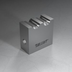 Talurit® The R - Combined Cylindrical Swaging Dies, a metal block featuring two grooves on the top and a hole on the side, commonly used in the mechanical splicing of wire rope, is placed on a textured surface. The word "TALURIT" is engraved on one side of the block. © Copyright Talurit AB. All rights reserved.