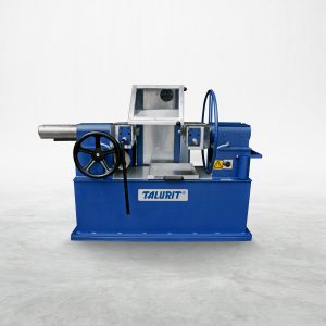 Talurit® A blue AV 65 - Annealing Machine with a silver cylindrical component on the left, a large black handwheel, a clear protective screen, and an encased electronic section. The brand name "TALURIT" is visible on the front, showcasing the precision of Talurit Group in wire rope and ferrule technology. The machine is on a plain, light surface. © Copyright Talurit AB. All rights reserved.