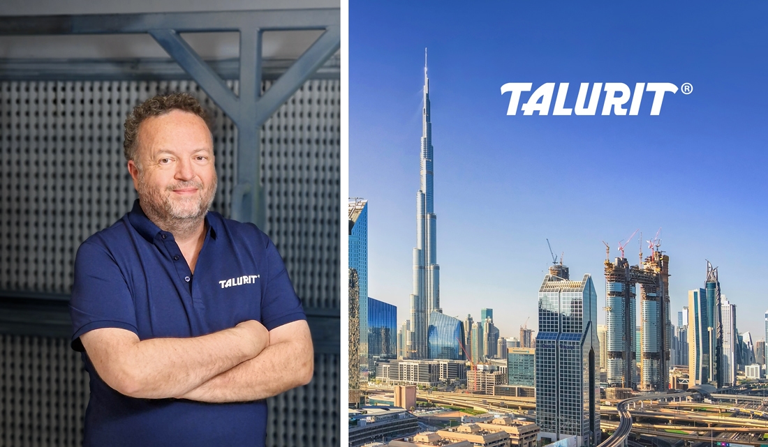 Talurit® Steve Hodgkins wearing a navy blue TALURIT polo shirt stands with arms crossed beside a cityscape featuring skyscrapers and the Burj Khalifa, highlighting Talurit Middle East, with the TALURIT logo above the buildings. © Copyright Talurit AB. All rights reserved.