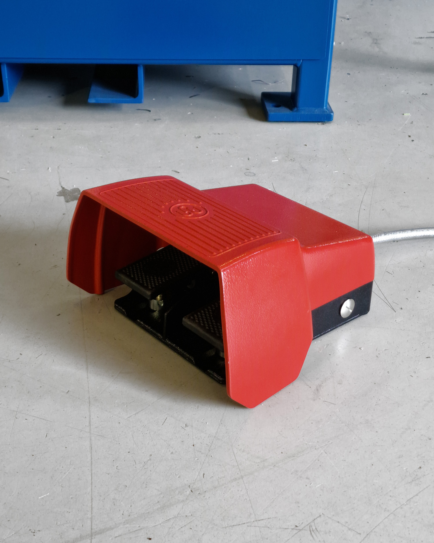 Talurit® A photo, featuring a red industrial foot pedal with a protective cover and connected by a cable, is positioned on a gray floor next to a 400T swager. © Copyright Talurit AB. All rights reserved.